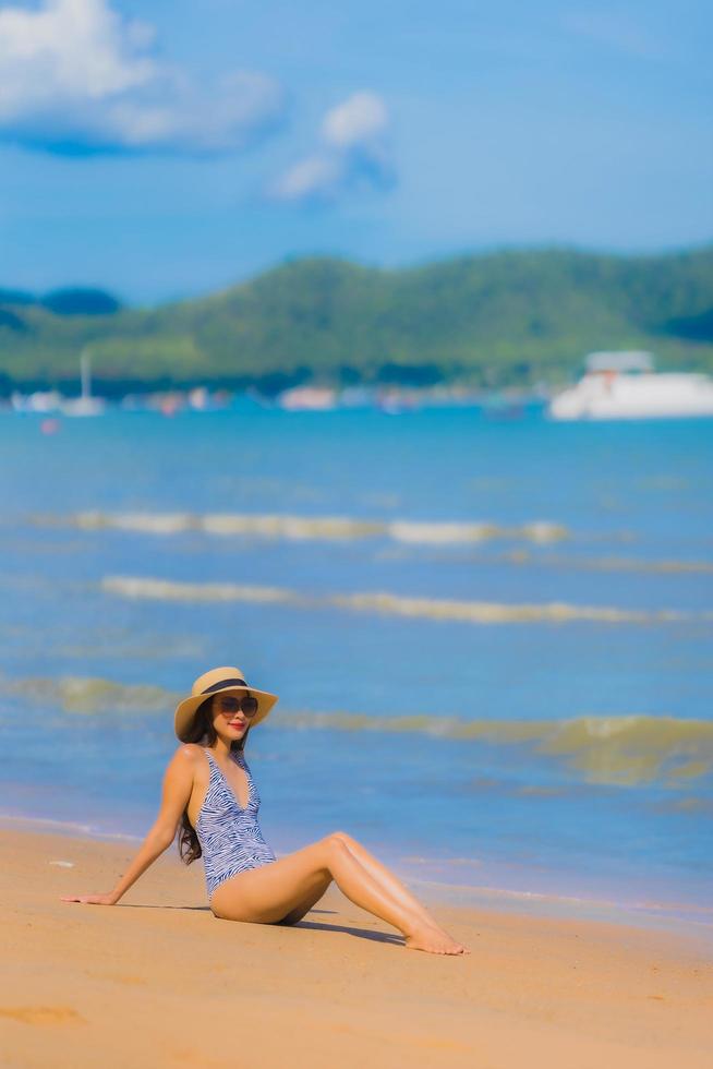 stående vacker ung asiatisk kvinna lyckligt leende koppla av på den tropiska stranden havet för fritidsresor foto