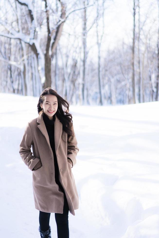 stående ung vacker asiatisk kvinna leende lycklig resa och njut av med snö vintersäsongen foto