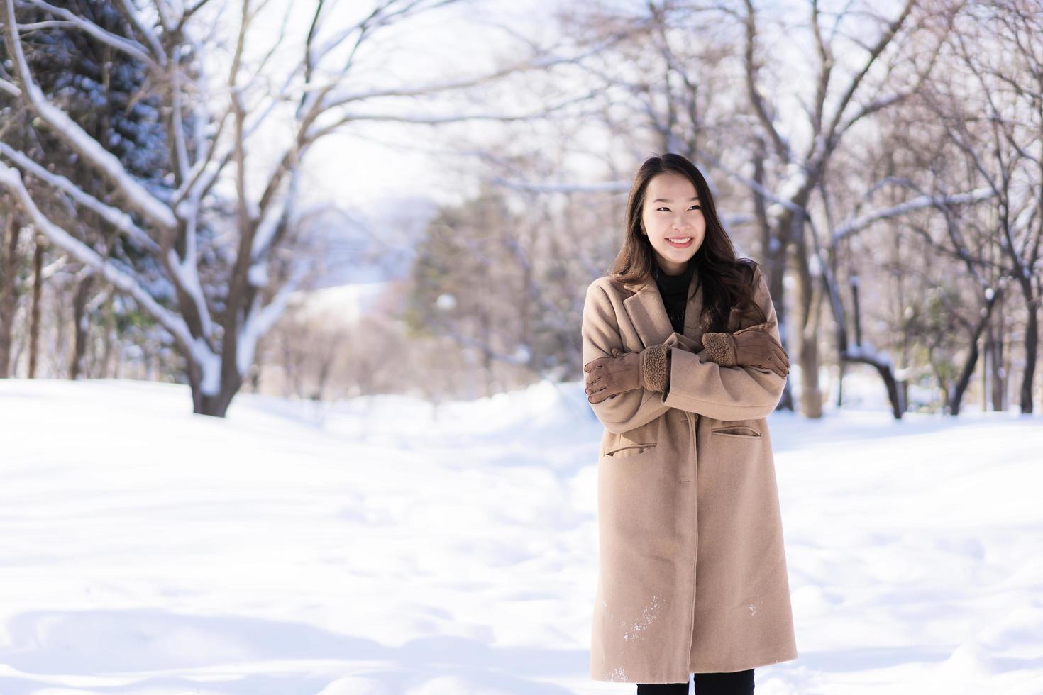 stående ung vacker asiatisk kvinna leende lycklig resa och njut av med snö vintersäsongen foto