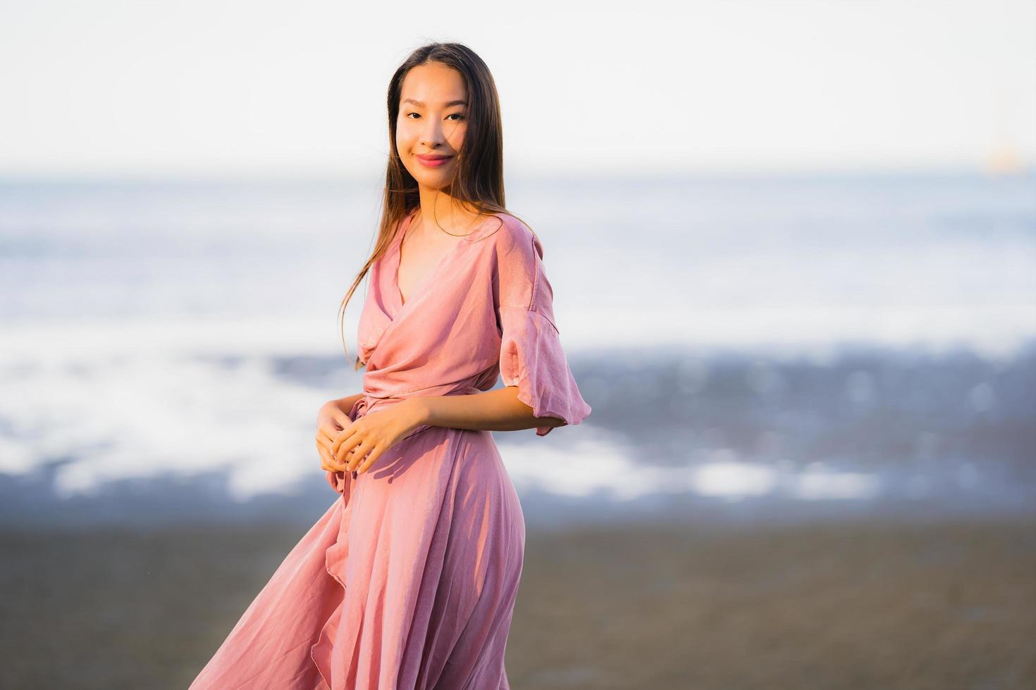 porträtt ung vacker asiatisk kvinna gå leende och glad på stranden havet och havet foto