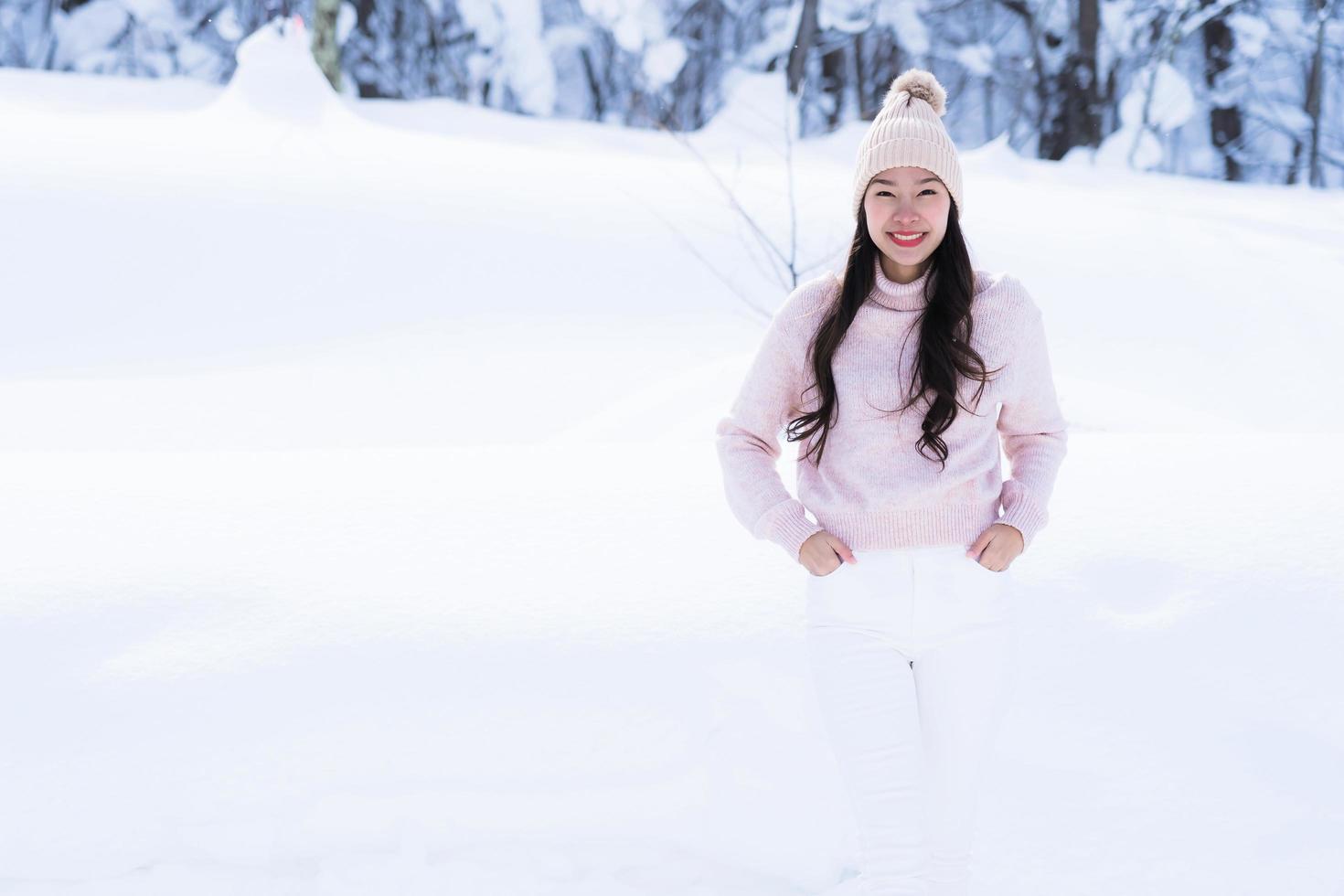 stående ung vacker asiatisk kvinna leende lycklig resa och njut av med snö vintersäsongen foto