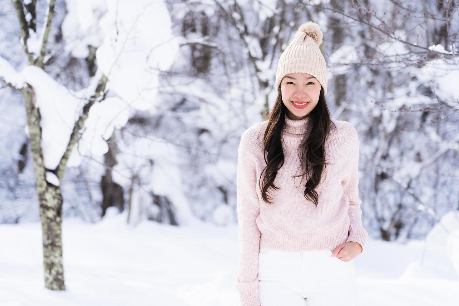 stående ung vacker asiatisk kvinna leende lycklig resa och njut av med snö vintersäsongen foto