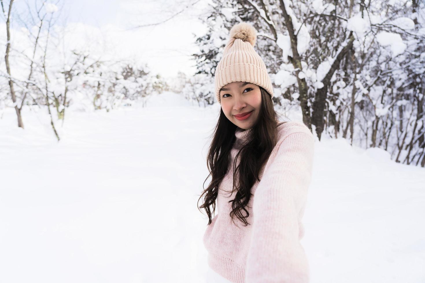 stående ung vacker asiatisk kvinna leende lycklig resa och njut av med snö vintersäsongen foto