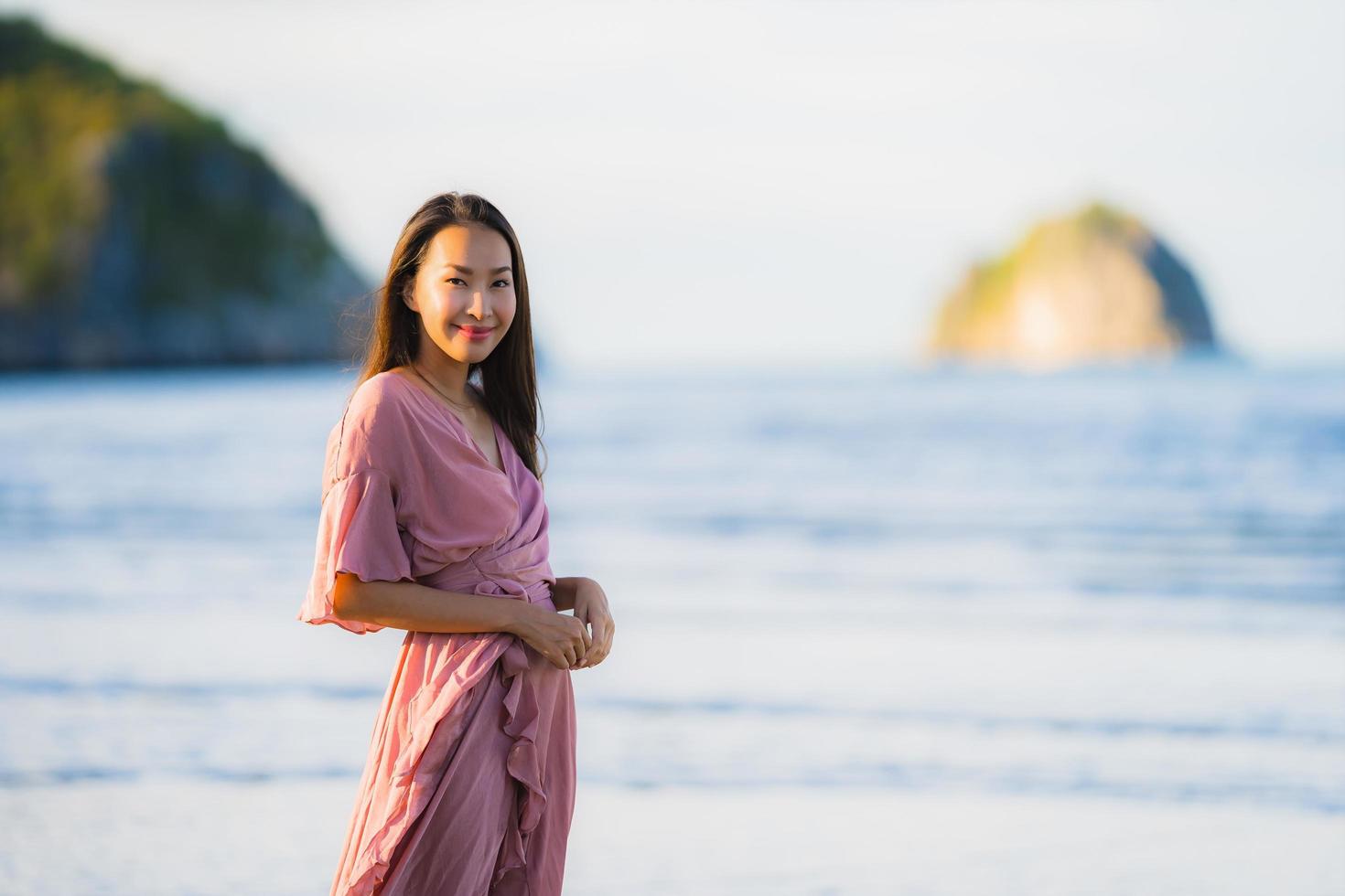 porträtt ung vacker asiatisk kvinna gå leende och glad på stranden havet och havet foto