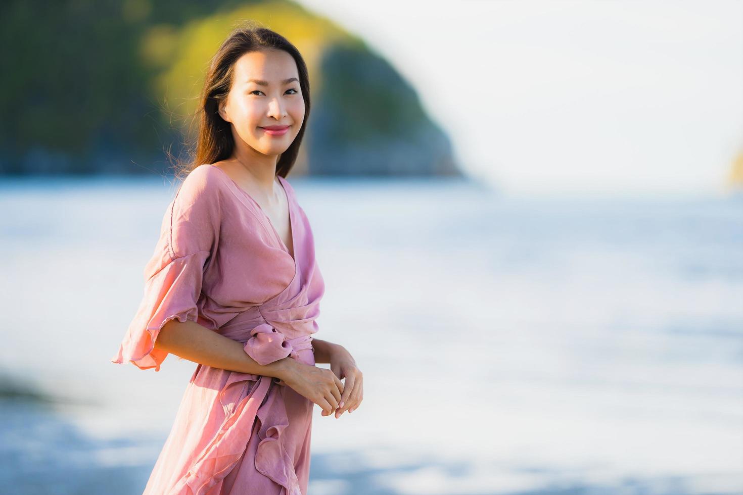 porträtt ung vacker asiatisk kvinna gå leende och glad på stranden havet och havet foto