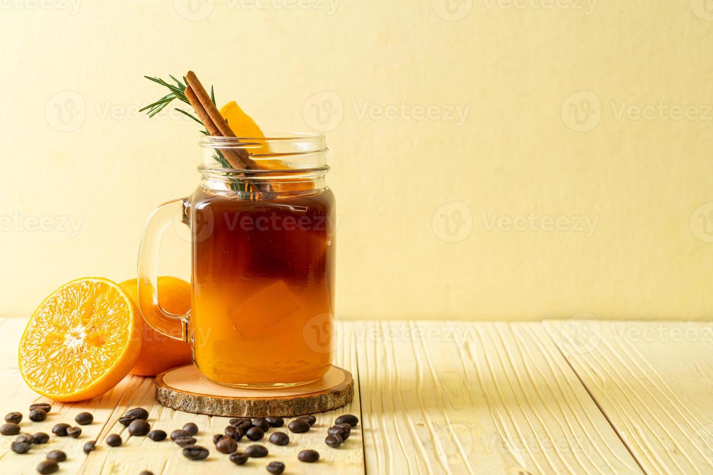 ett glas iced americano svart kaffe och ett lager apelsin- och citronsaft dekorerad med rosmarin och kanel på träbakgrund foto