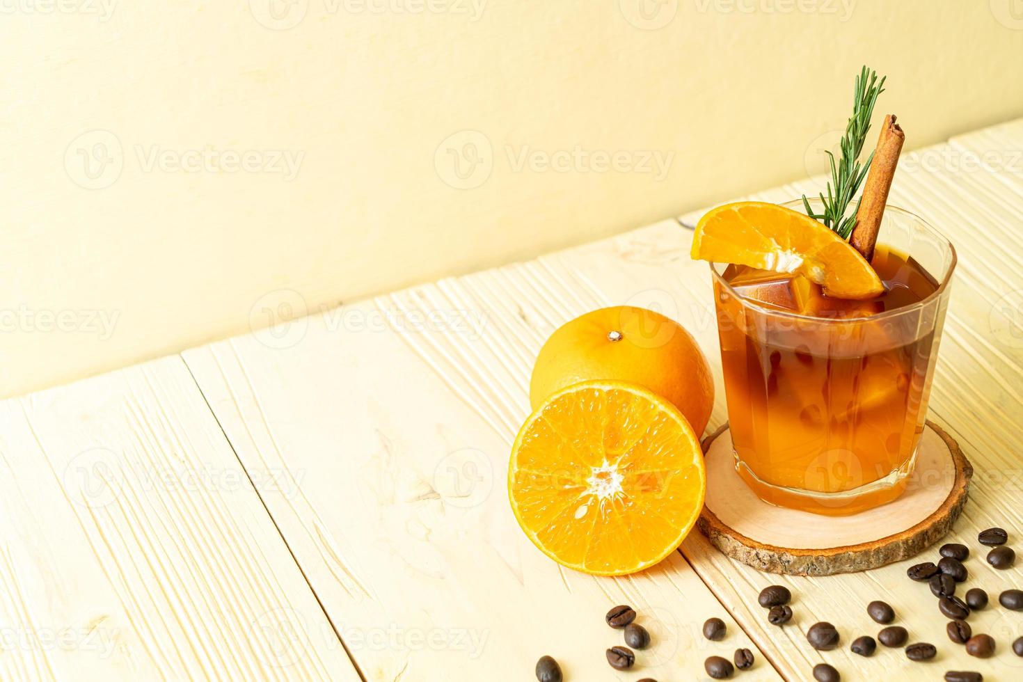 ett glas iced americano svart kaffe och ett lager apelsin- och citronsaft dekorerad med rosmarin och kanel på träbakgrund foto