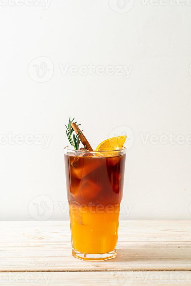 ett glas iced americano svart kaffe och ett lager apelsin- och citronsaft dekorerad med rosmarin och kanel på träbakgrund foto