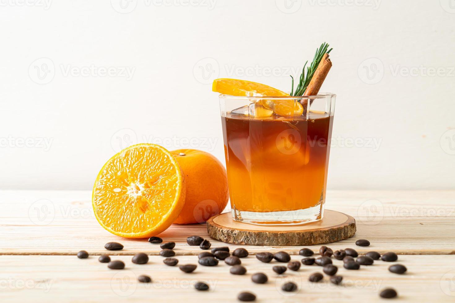 ett glas iced americano svart kaffe och ett lager apelsin- och citronsaft dekorerad med rosmarin och kanel på träbakgrund foto