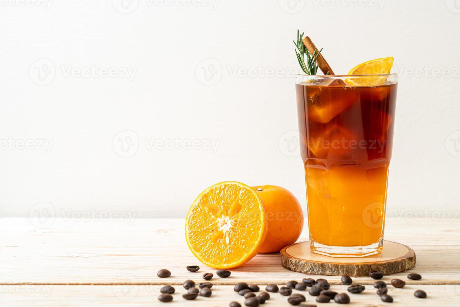 ett glas iced americano svart kaffe och ett lager apelsin- och citronsaft dekorerad med rosmarin och kanel på träbakgrund foto