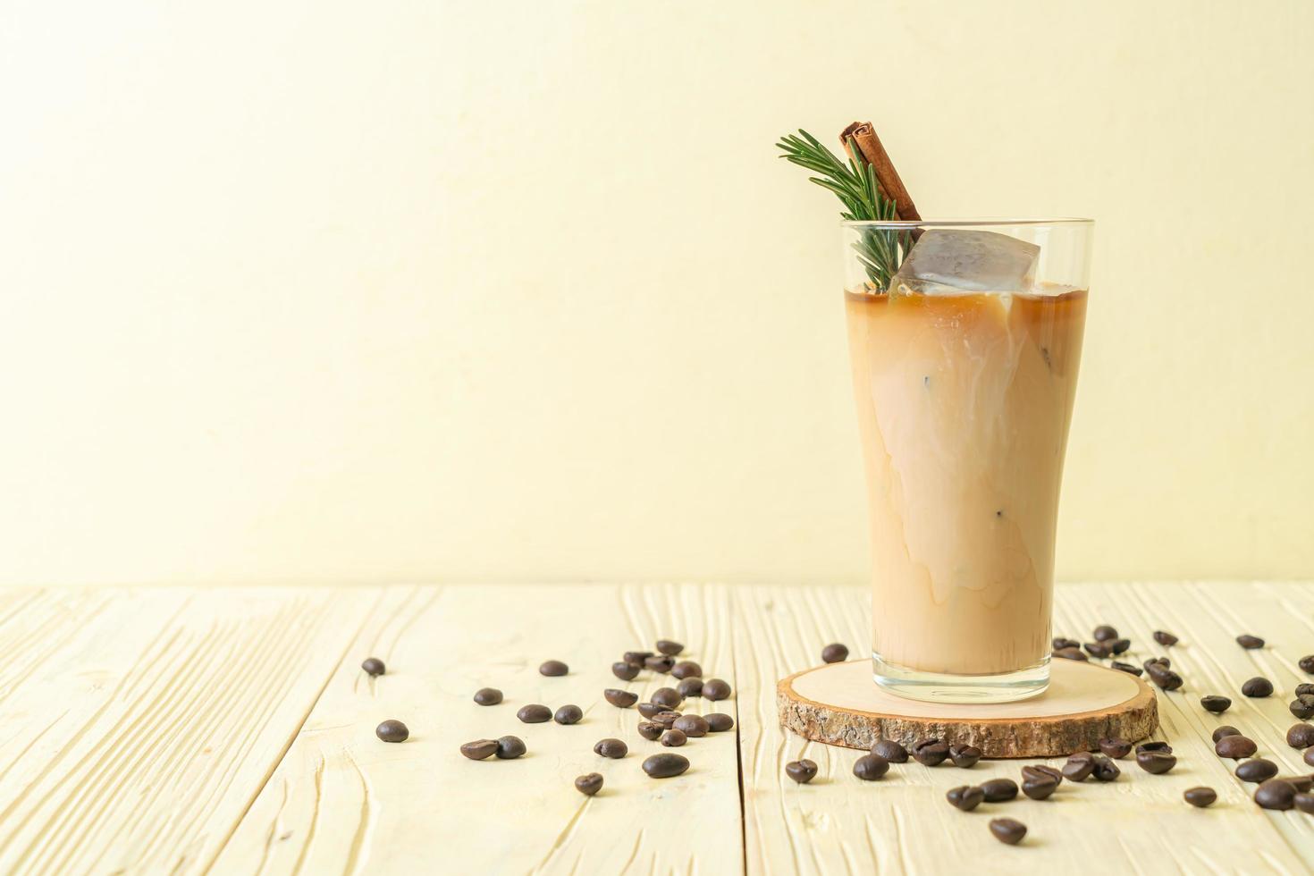 hälla mjölk i svart kaffeglas med isbitar, kanel och rosmarin på träbakgrund foto