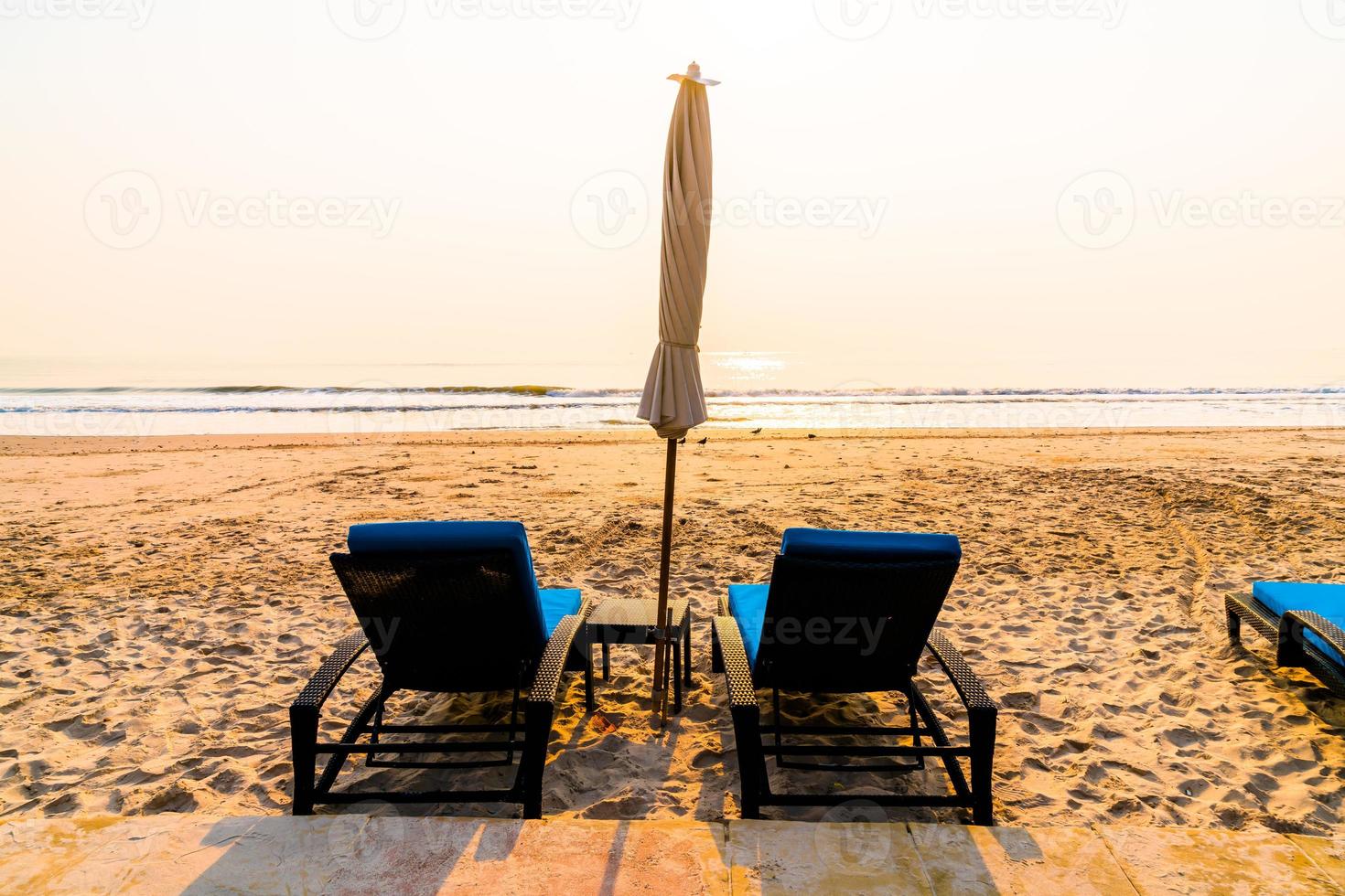paraplystrandstol med palmträd och havsstrand vid soluppgångstid - semester- och semesterkoncept foto