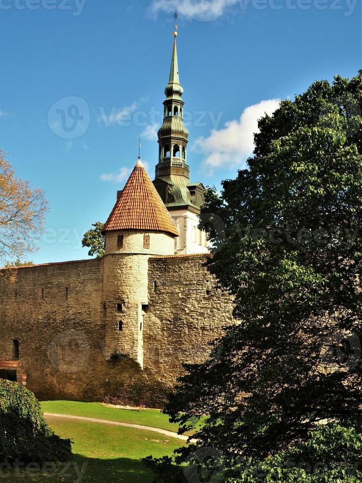 klocktorn i kyrkan St Nicholas i Tallinn Estland sett bakom ett torn i stadsmuren foto