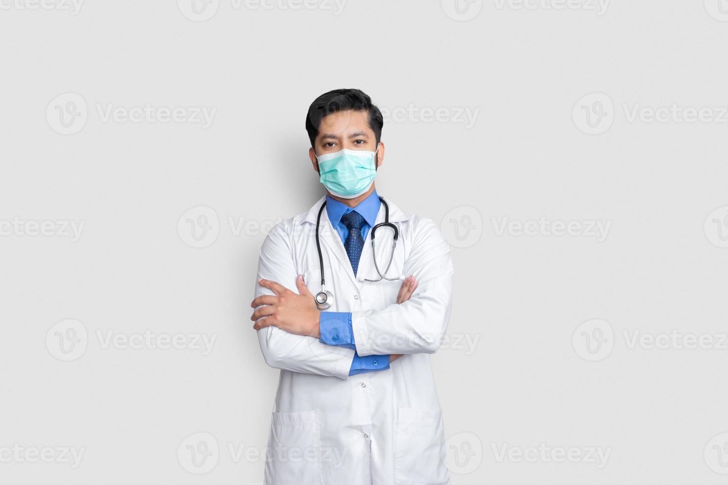 ung manlig läkare ansikte täckt med mask och arm korsar över isolerad bakgrund, hälsokoncept foto