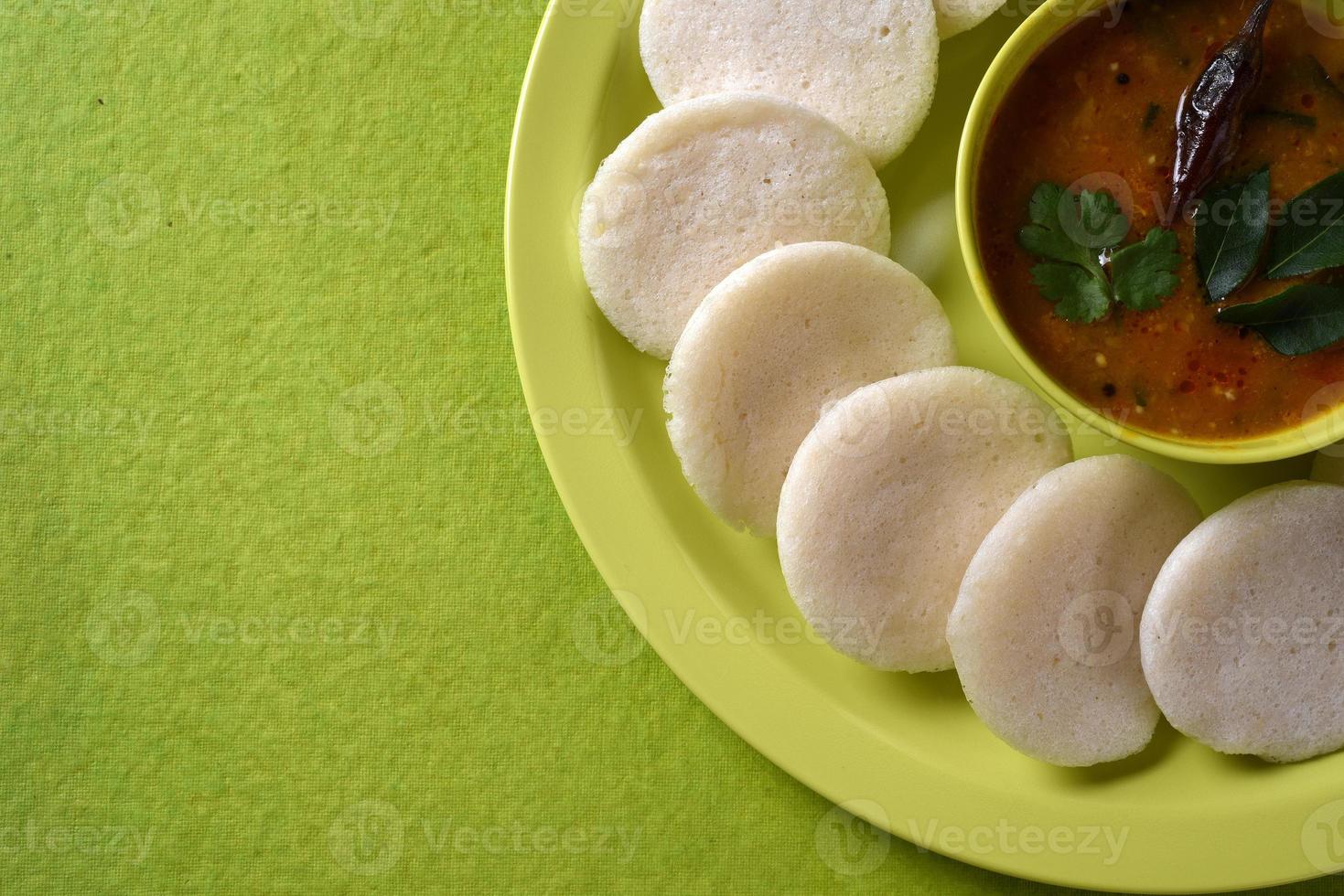 idli med sambar i skål på grön bakgrund, indisk maträtt sydindisk favoritmat rava idli eller semolina idly eller rava idly, serveras med sambar och grön kokosnötchutney. foto