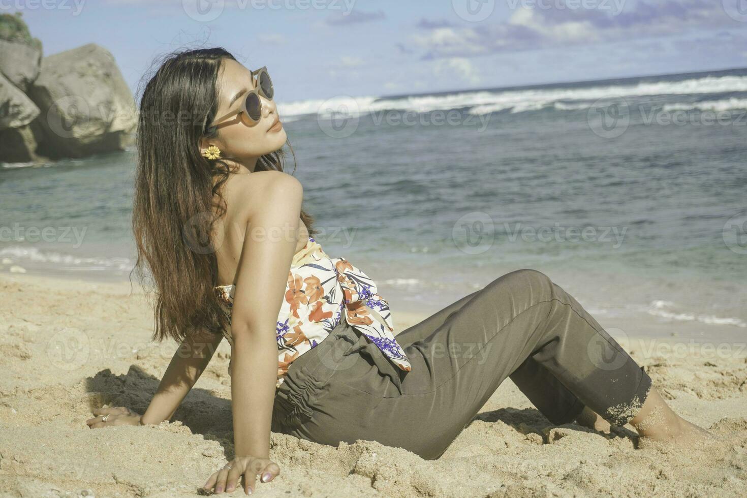 ung asiatisk kvinna sitta på de strand sand. porträtt sexig asiatisk lady reser och avkopplande i de sommar med tropisk natur. foto