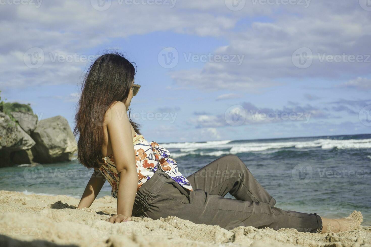 ung asiatisk kvinna sitta på de strand sand. porträtt sexig asiatisk lady reser och avkopplande i de sommar med tropisk natur. foto