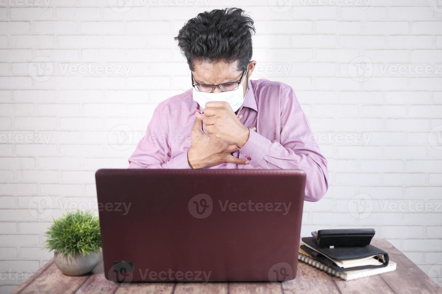 ung asiatisk man hostar och nysar medan han sitter på skrivbordet foto