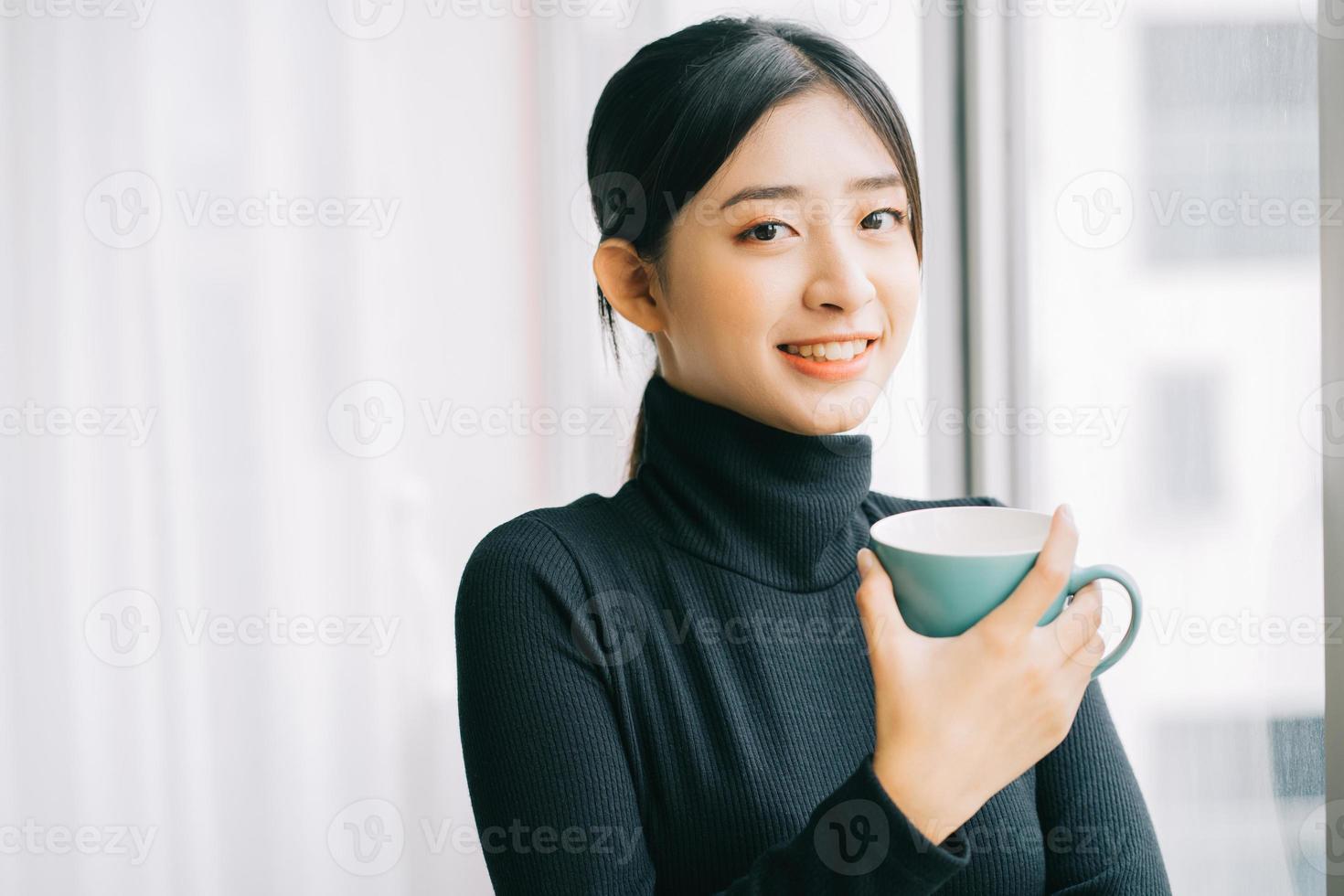 asiatisk kvinna som dricker kaffe vid fönstret under pausen foto