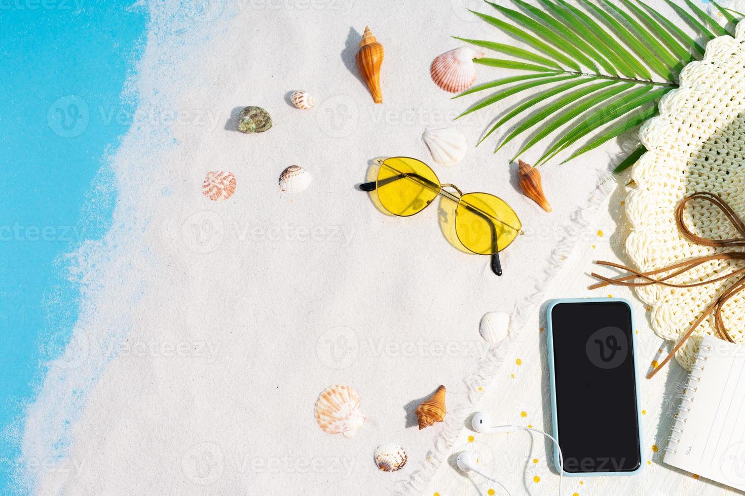 telefonen placeras på sanden med snäckskal och solglasögon runt foto