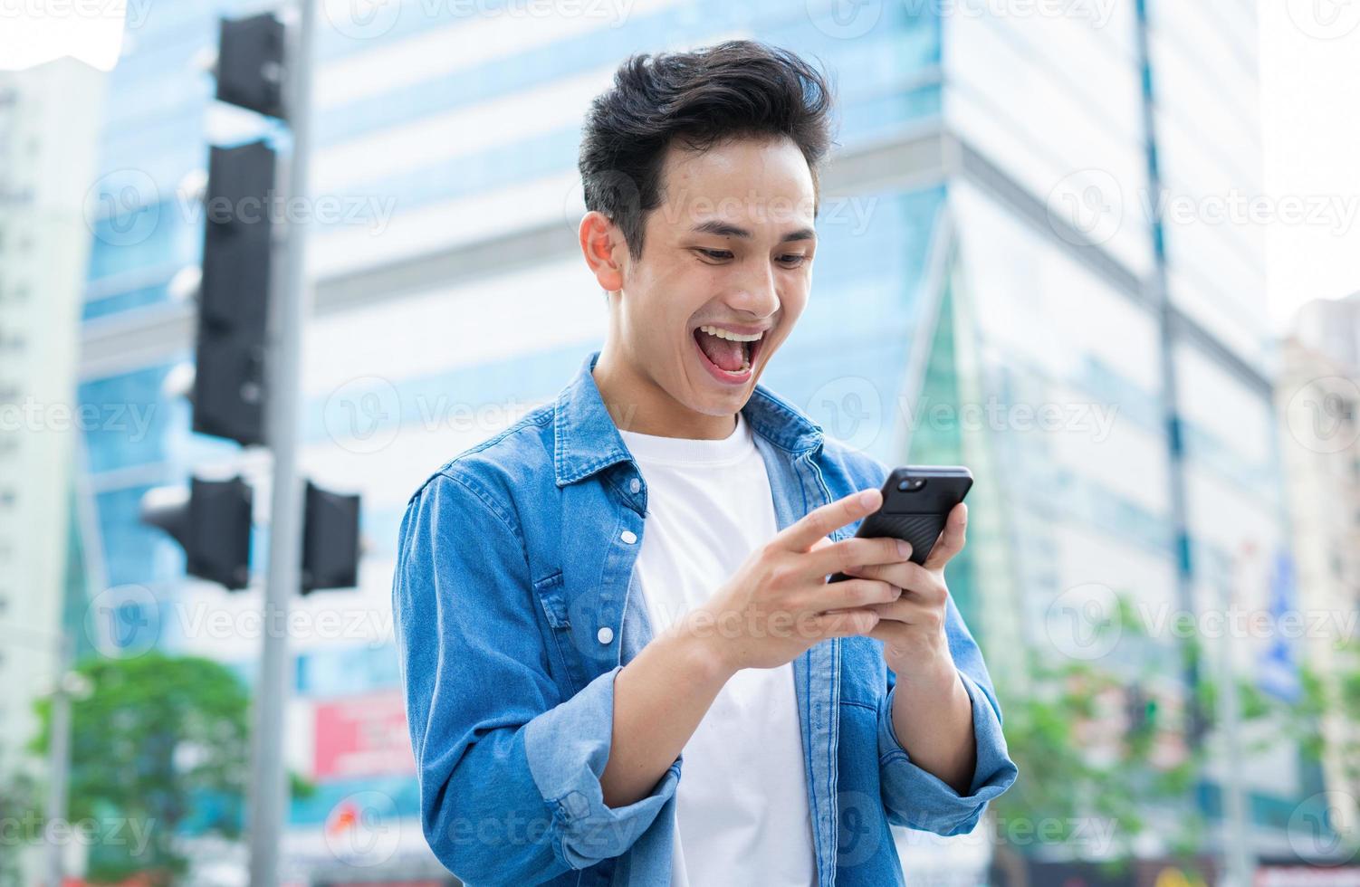 ung asiatisk man som använder smartphonen medan han går på gatan foto