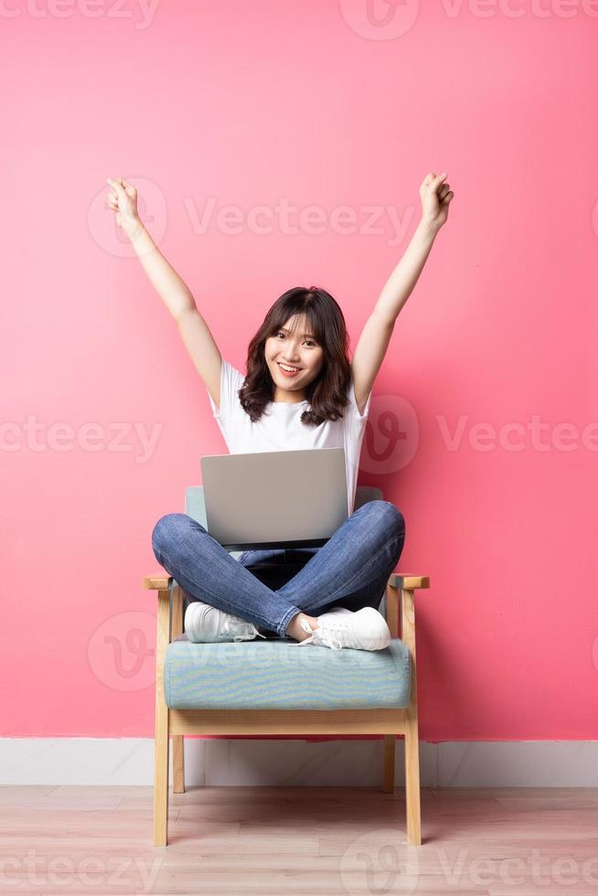asiatisk kvinna som sitter på soffan med bärbar dator med lyckligt uttryck foto