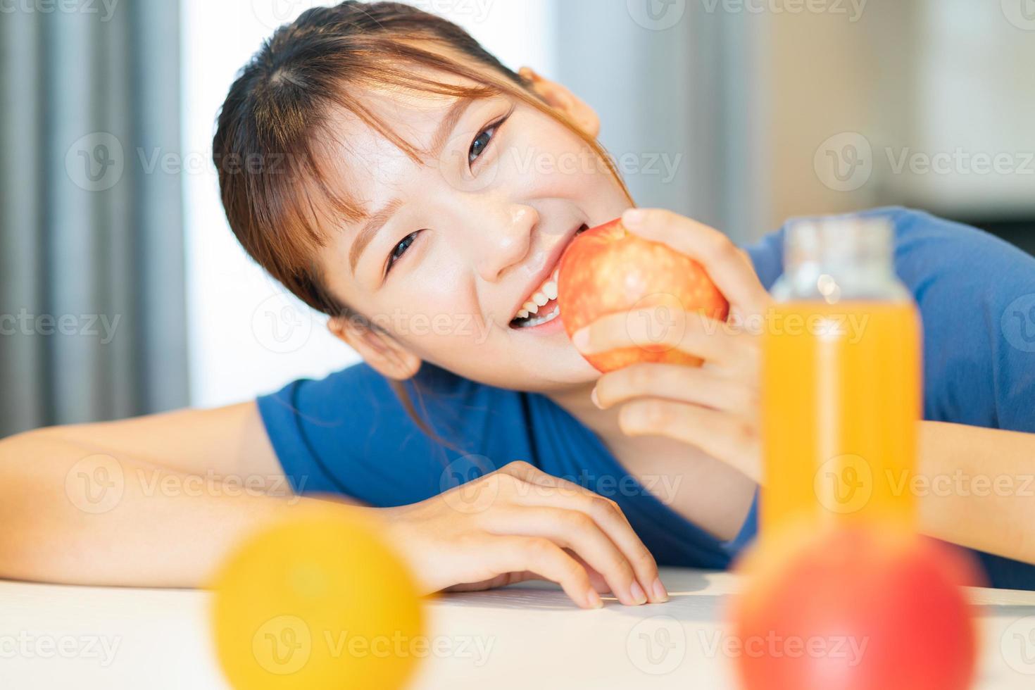 en ung asiatisk kvinna som äter frukost med frukt i sitt kök foto