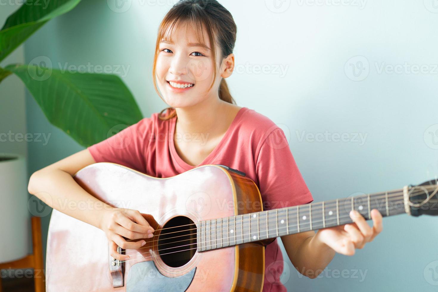 ung asiatisk kvinna som lär sig gitarr hemma foto