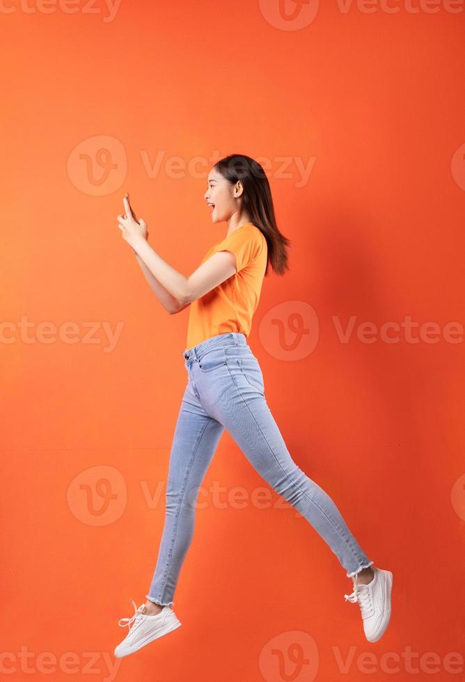 ung asiatisk kvinna som bär orange t-shirt hoppar på orange bakgrund foto