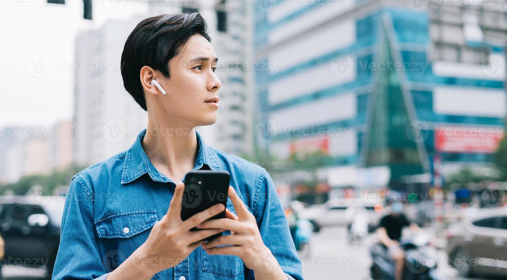 ung asiatisk man går och använder smartphone på gatan foto