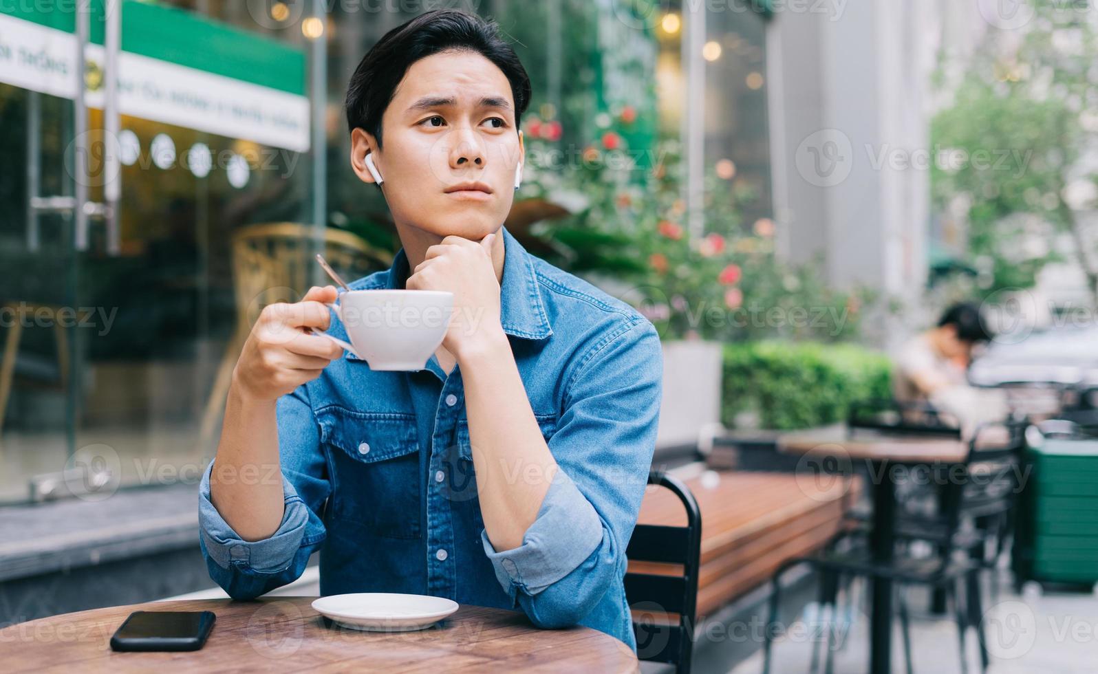 ung asiatisk man sitter fundersamt medan han dricker kaffe foto