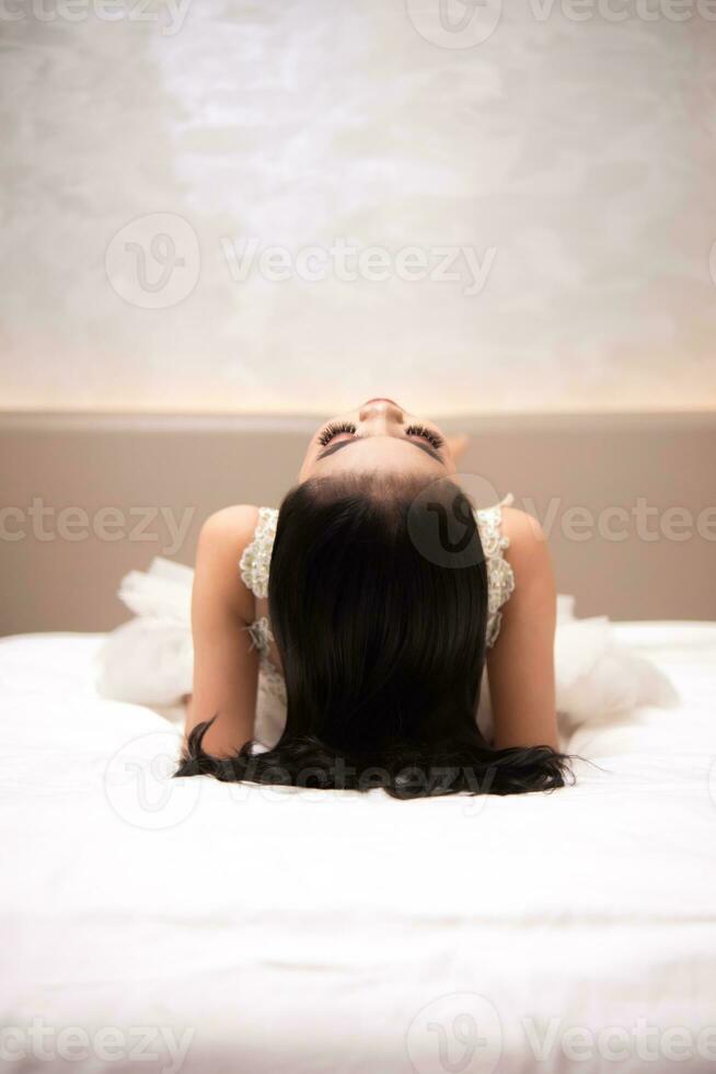 ett asiatisk kvinna med svart hår är sovande på en vit säng i ett elegant hotell foto