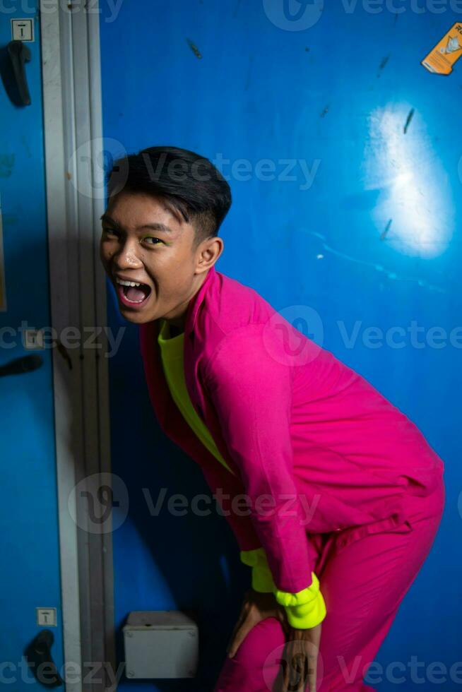 en Gay asiatisk man Framställ mycket rolig och humoristisk medan bär en rosa kostym i främre av en blå bakgrund foto