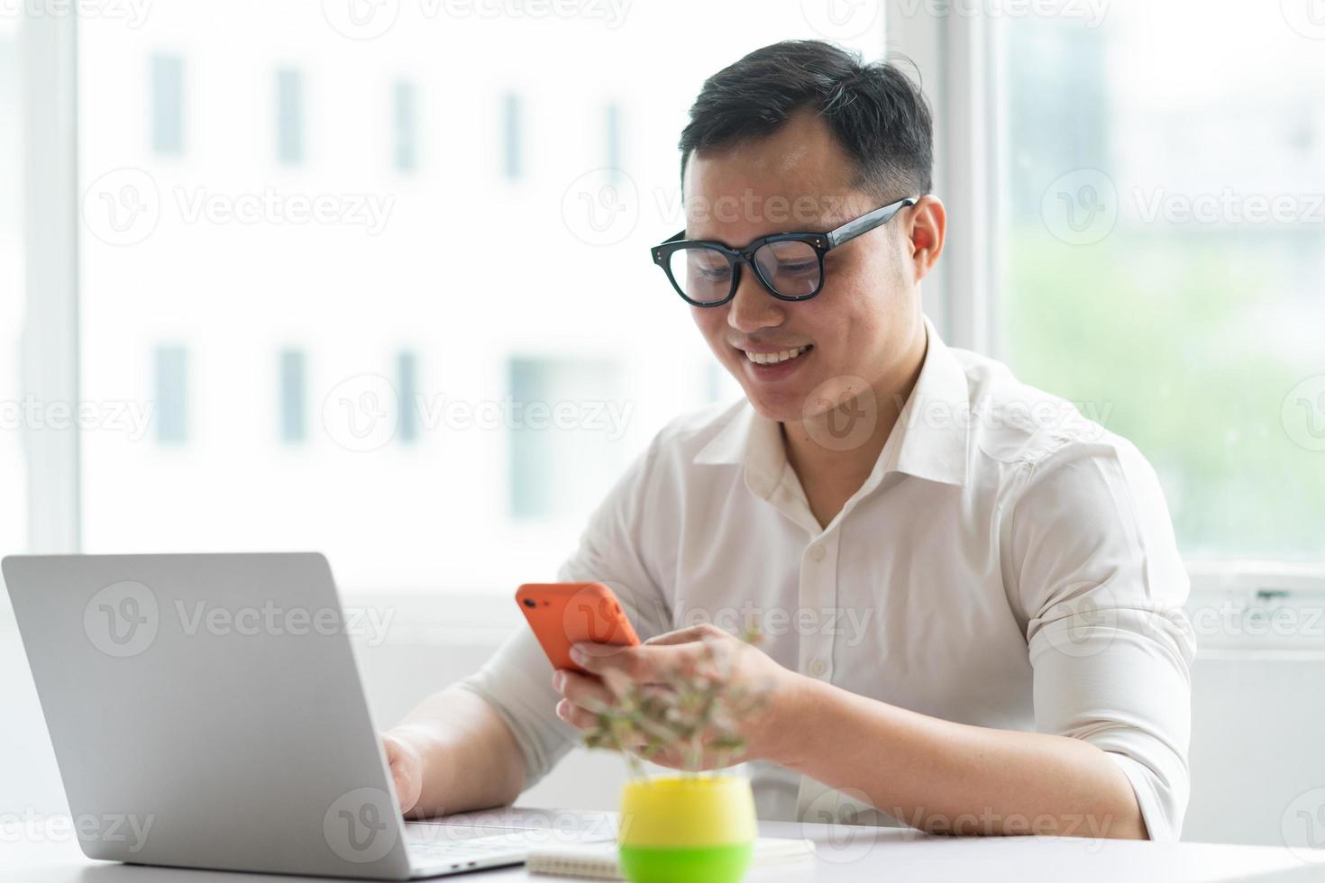 ung asiatisk affärsman som använder smartphonen och bärbara datorn på kontoret foto