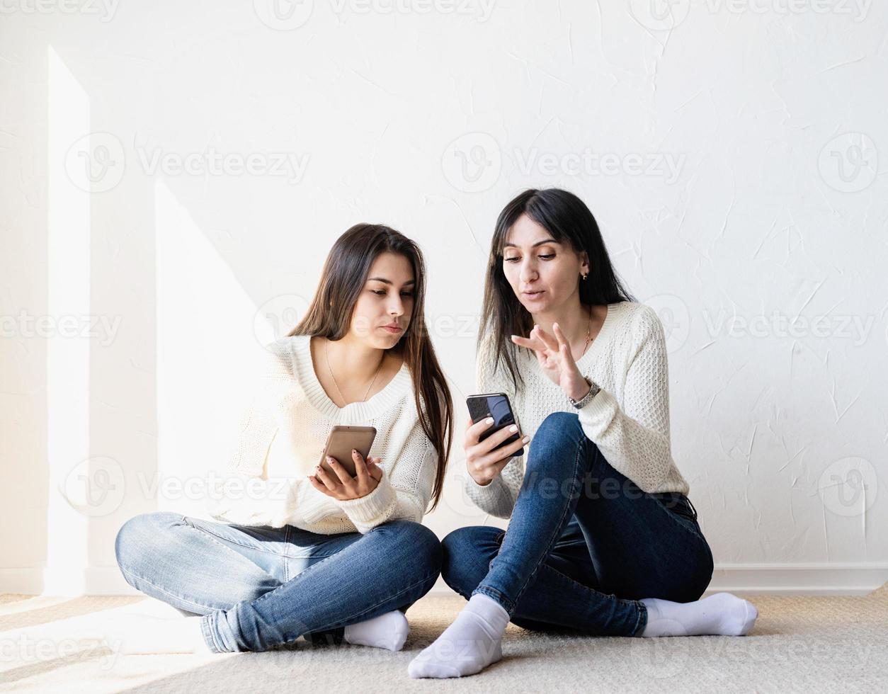 två vackra kvinnavänner som skickar meddelanden med mobiltelefoner foto