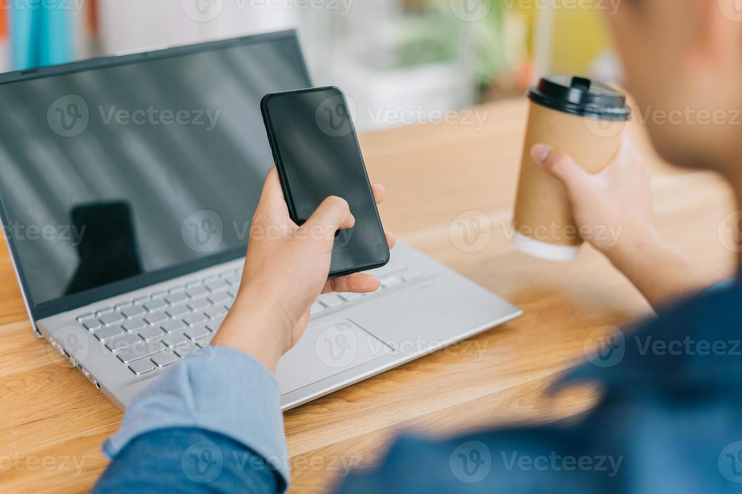 asiatisk man som håller smartphonen och använder bärbar dator foto