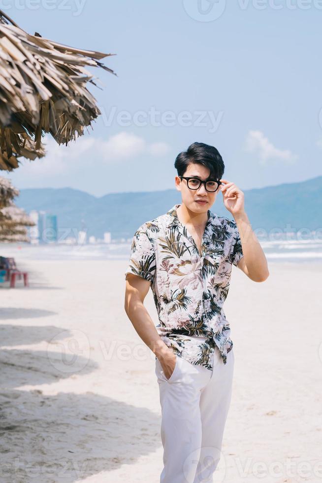 ung asiatisk man som går på stranden foto