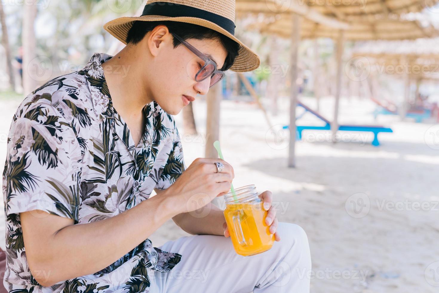 ung asiatisk man som dricker apelsinjuice på stranden foto