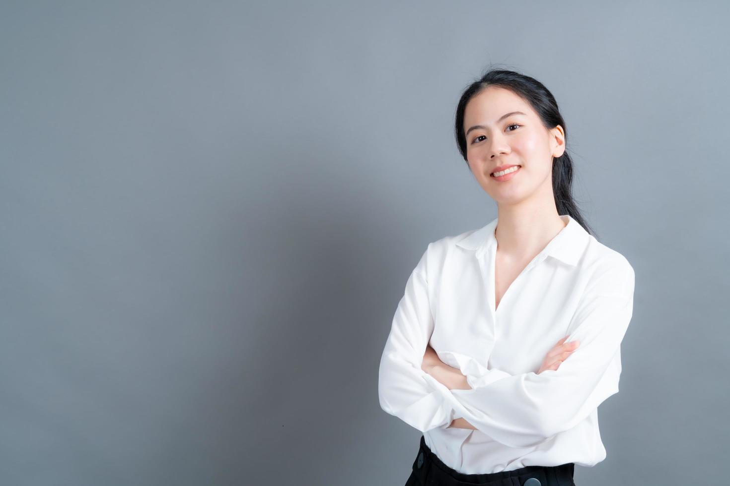 glad asiatisk kvinna med lyckligt ansikte i vit skjorta på grå bakgrund foto