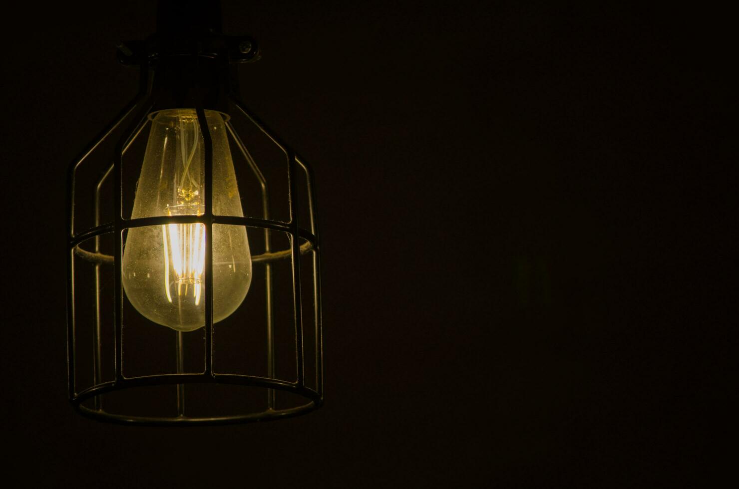 natt fotografi av de ljus Glödlampa, glödande lampa, en tråd tråd den där är uppvärmd fram tills den lyser. med metall bur isolerat på svart bakgrund. foto