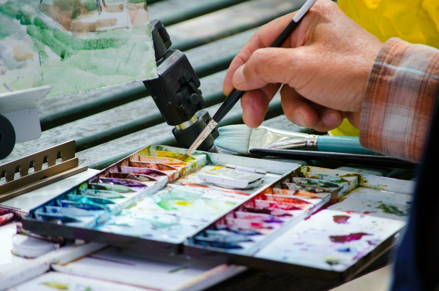 en mannens hand innehav de paintbrush och blandning Färg på måla palett, i stänga upp foto