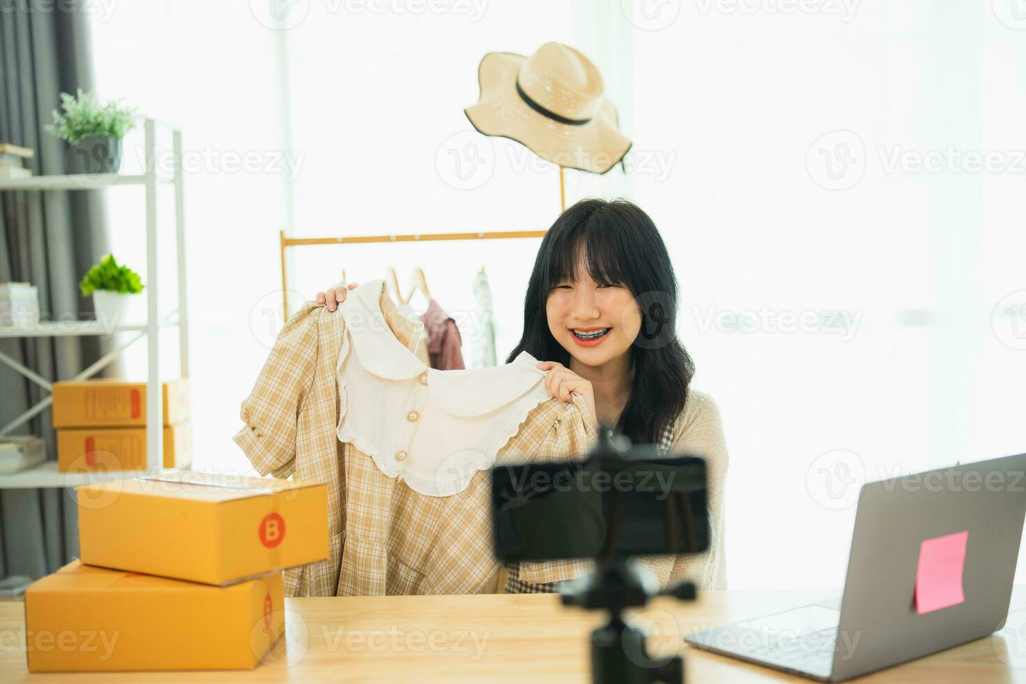 asiatisk kvinna ångande sälja trasa skjorta produkt uppkopplad leva på Hem. ung kvinna använder sig av mobil telefon video ring upp visar varor till kund och detalj. handla uppkopplad e-handel uppköp och försäljning begrepp. foto