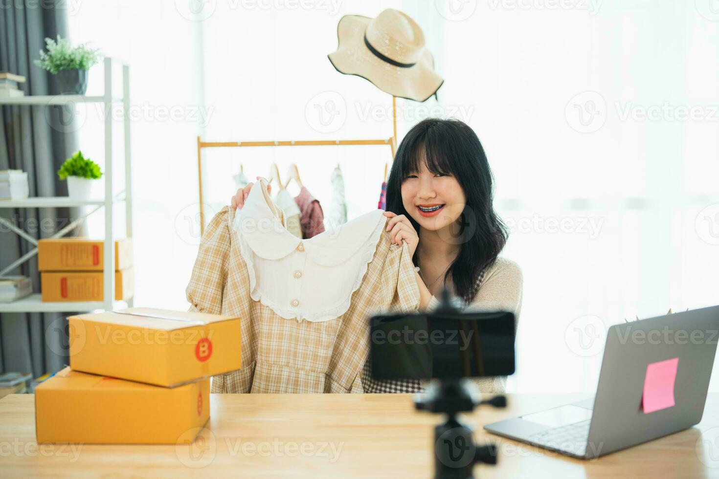 asiatisk kvinna ångande sälja trasa skjorta produkt uppkopplad leva på Hem. ung kvinna använder sig av mobil telefon video ring upp visar varor till kund och detalj. handla uppkopplad e-handel uppköp och försäljning begrepp. foto