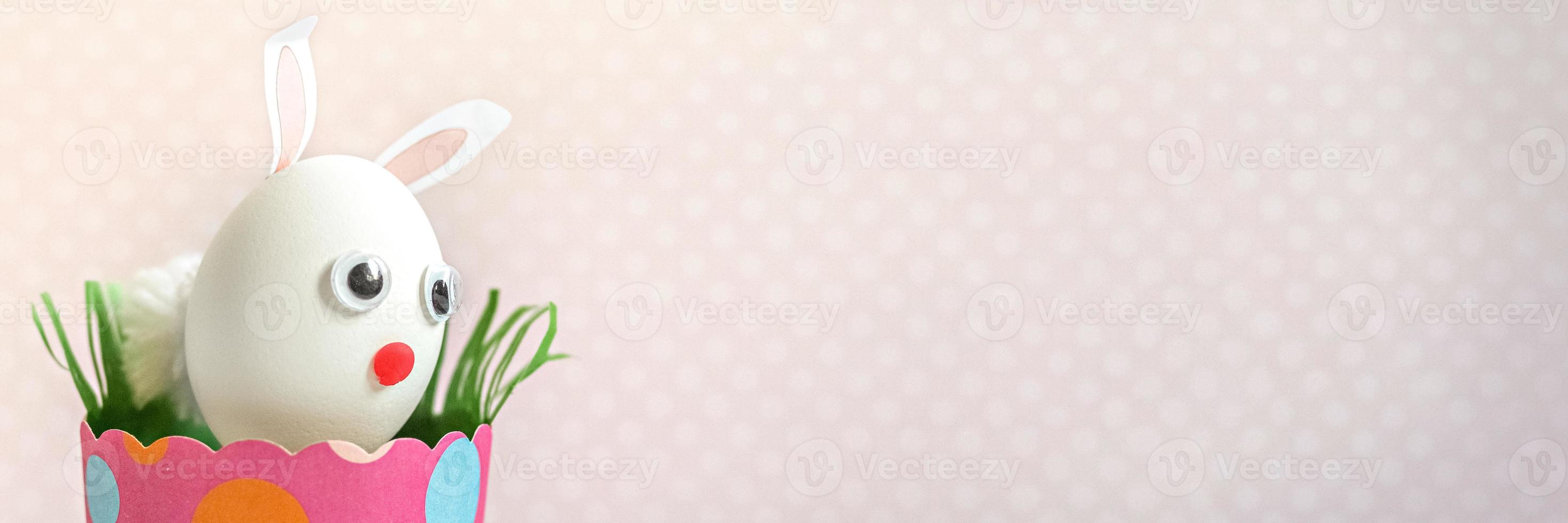 vitt kycklingägg med kaninöron och en munkorg i ett miljövänligt rosa pappersfack, låda. glad påskhelg koncept. banner foto