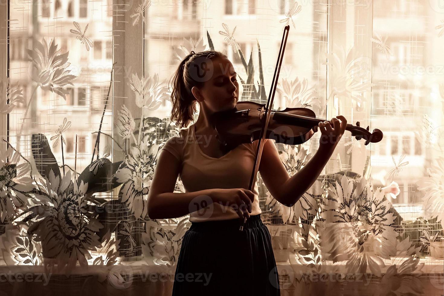 silhuett av en ung flicka, en musiker. spelar fiol i fönstrets bakgrund foto