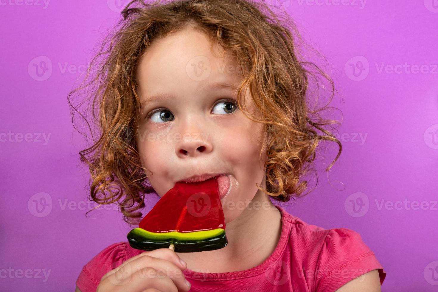 barn njuter av vattenmelon klubba, söt liten flicka slickar godis foto