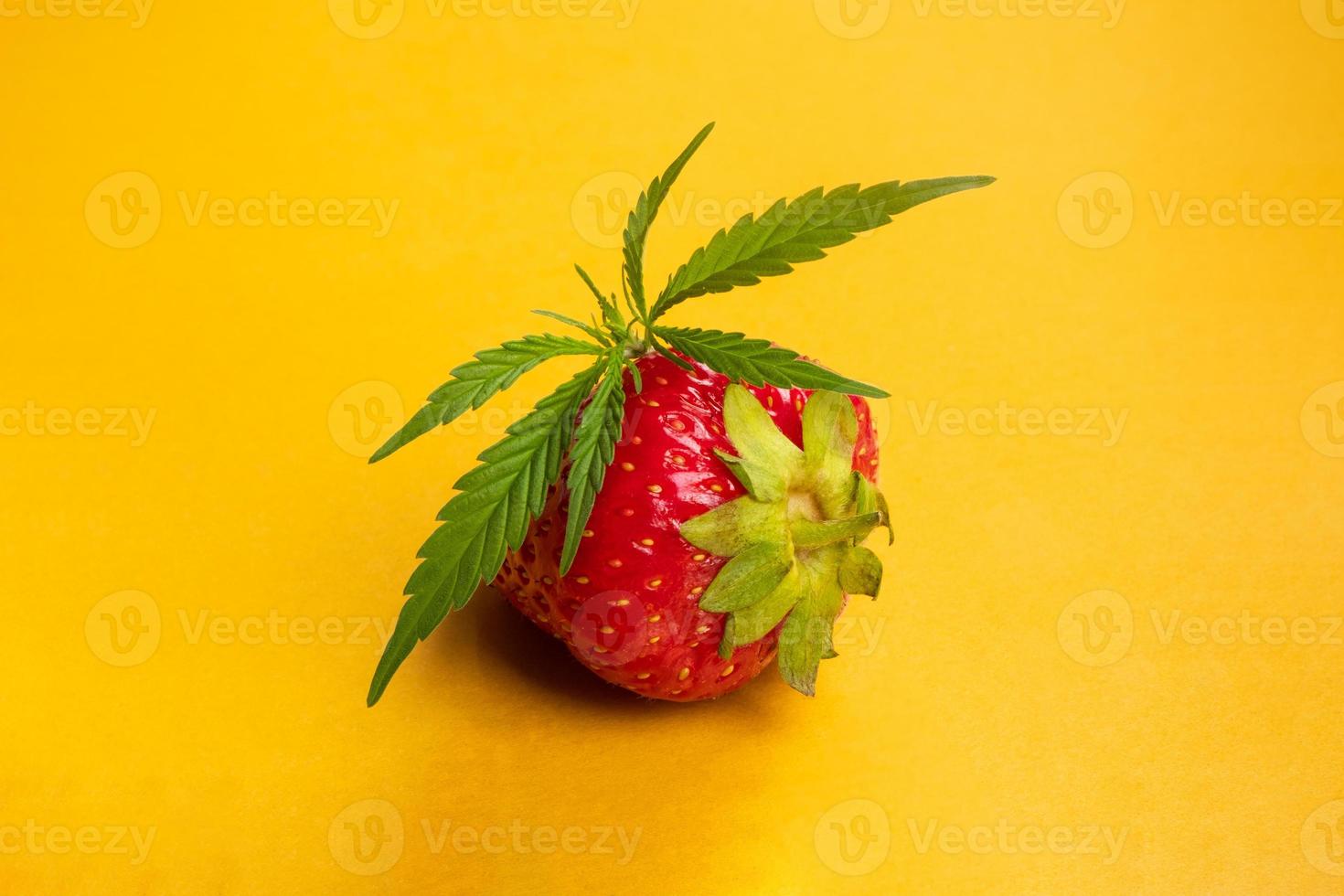 färsk jordgubbe med marijuanablad på gul bakgrundsnärbild, cannabisvariant med jordgubbsdoft foto