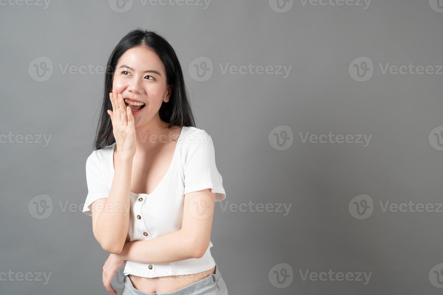 ung asiatisk kvinna med lyckligt och leende ansikte i vit skjorta på grå bakgrund foto