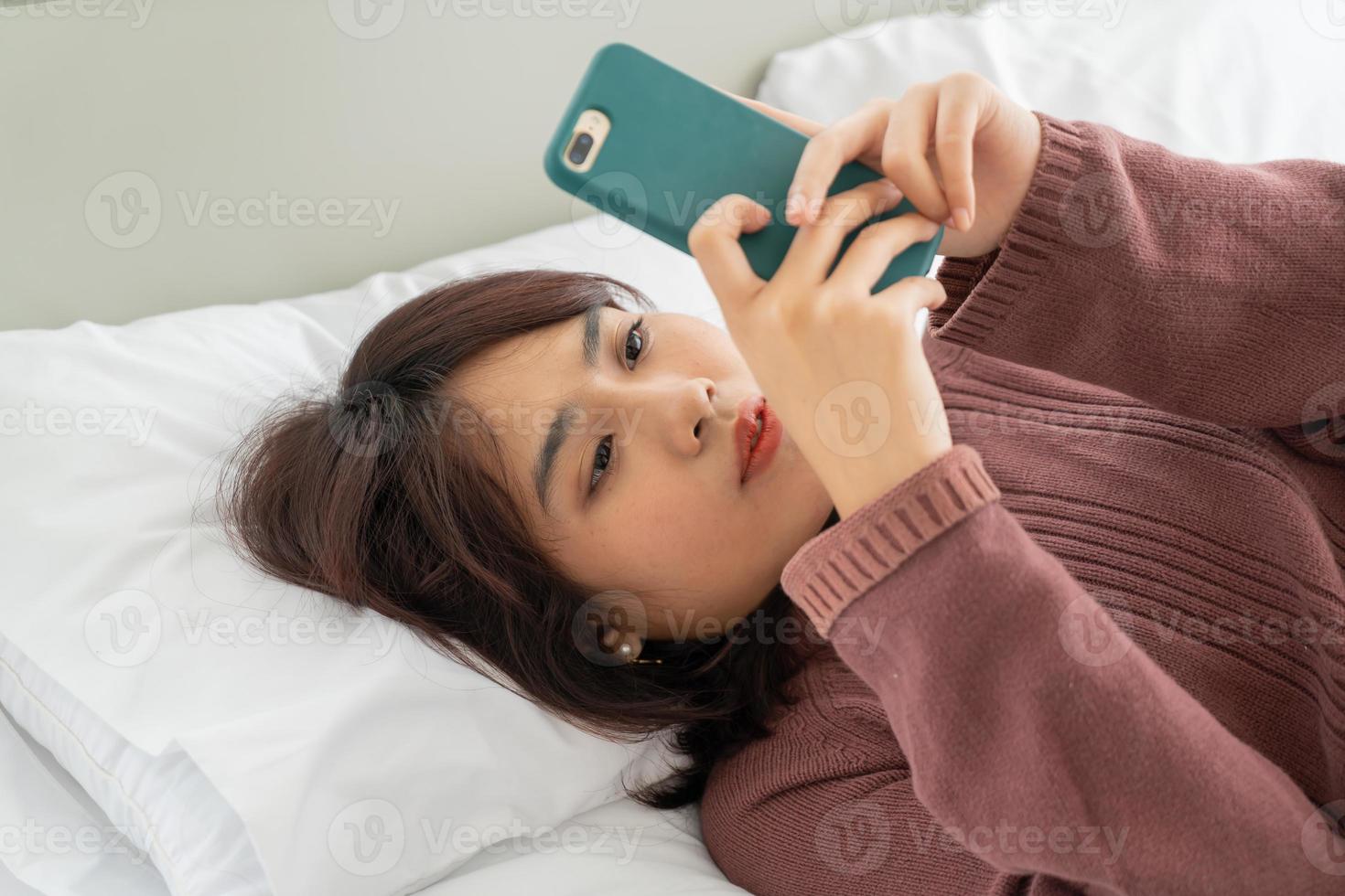 asiatisk kvinna som spelar smartphone på sängen foto