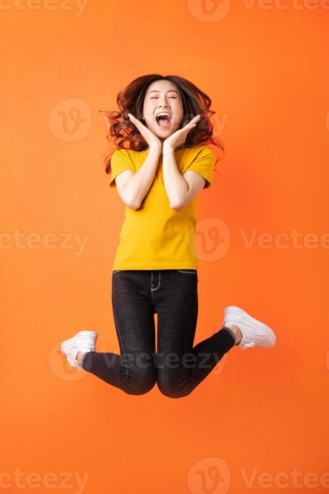 ung asiatisk kvinna som hoppar upp på orange bakgrund foto